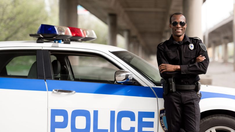 Police Officer Leaning On Cop Car Under Bridge